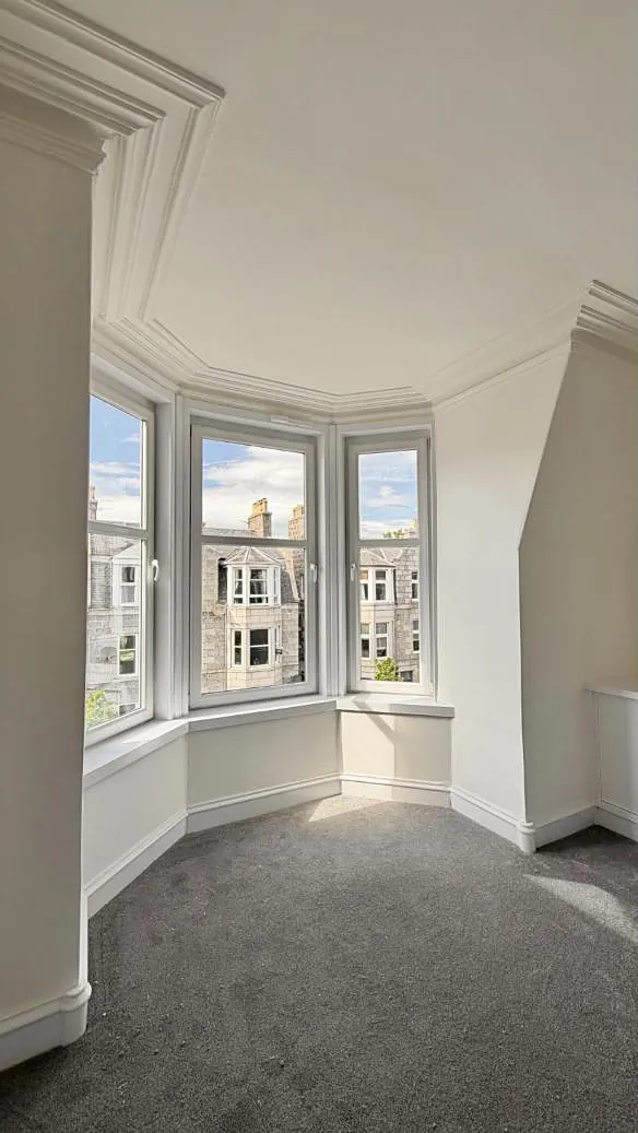 A freshly painted room with a three-pane bay window looking out over granite tenements on Union Grove