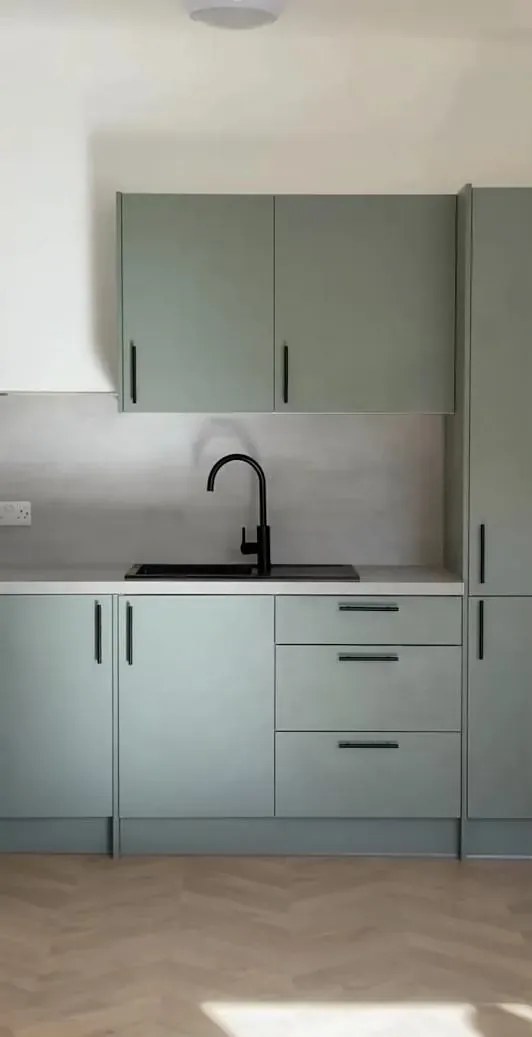 A newly fitted sage shaker kitchen with black handles, a black tap and a herringbone floor